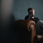 Mental Health - a man holds his head while sitting on a sofa