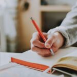 Journaling - person holding on red pen while writing on book