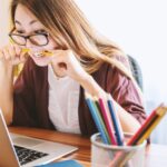 Stress - woman biting pencil while sitting on chair in front of computer during daytime