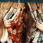 Thrift Shopping - person holding assorted clothes in wooden hanger